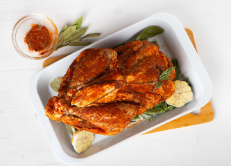 Raw guinea fowl smeared with spices with paprika lies on a white dish for baking with garlic and rosemary