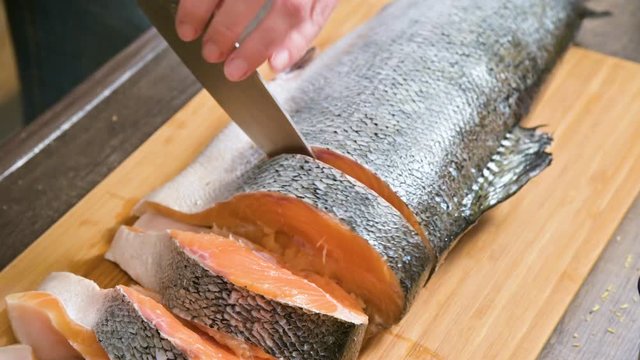 Close-up of female hands are cutting with a knife a large salmon on a wooden table of home cooking