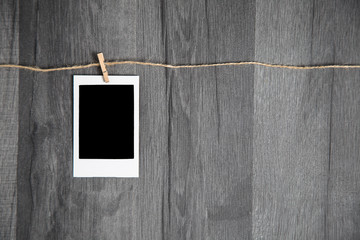 Blank vintage polaroid instant photo with empty space hanging on rope on wooden background