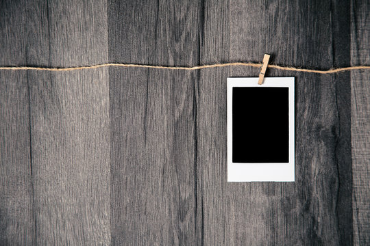 Blank vintage polaroid instant photo with empty space hanging on rope on wooden background