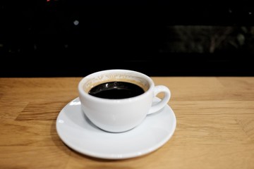 Hot espresso coffee in a white cup on wooden dinning table at night, coffee cafe area 