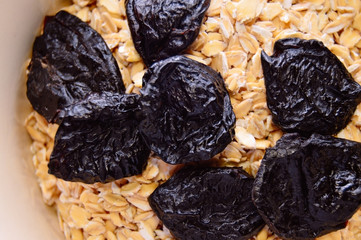 Dried prunes and oatmeal in a bowl. Top view. Close-up.