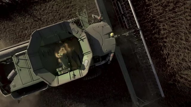 Aerial footage of a green combine tractor harvesting grains in a large field.