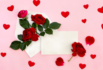 Decoration of Valentine Day. Beautiful flowers red roses in postal envelope and blank sheet with space for text and red petal roses on a pink paper background with hearts. Top view, flat lay