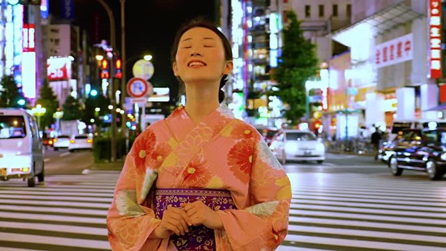 Attractive Japanese woman in a kimono waiting. Traffic and the lights of Shinjuku are behind her.