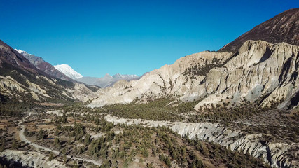 A harsh mountains slopes on the way to Humde, Annapurna Circus Trek, Himalayas, Nepal. Captured with a drone, from above.Beautiful clear blue sky. in the back white mountain peaks visible.