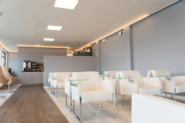 empty Lounge area with white chairs, grey wall and coffee maker in the rear 