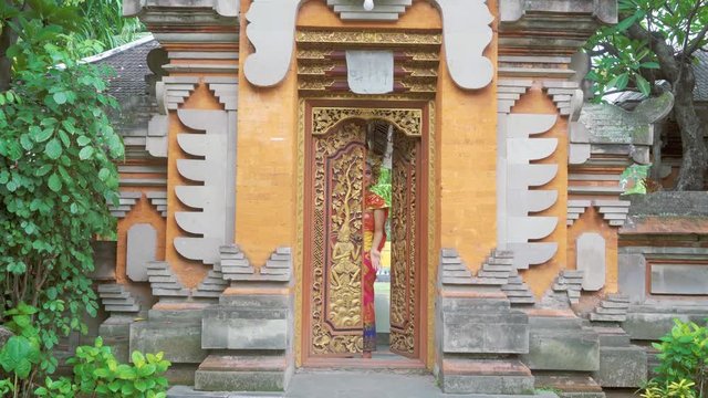 Beautiful balinese woman coming out from a traditional balinese door while wearing traditional clothes and smiling at the camera. Shot in 4k resolution