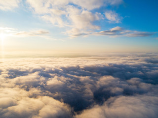 Naklejka na ściany i meble Aerial view White clouds in blue sky. Top view. View from drone. Aerial bird's eye view. Aerial top view cloudscape. Texture of clouds. View from above. Sunrise or sunset over clouds
