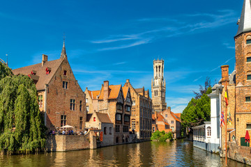 Fototapeta na wymiar The Rozenhoedkaai canal in Bruges with the belfry in the background. Typical view of Bruges (Brugge), Belgium with red brick houses with triangle shaped roofs and canals.