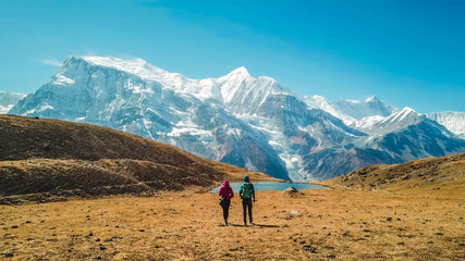 Een paar dat naar het ijsmeer loopt, als onderdeel van de Annapurna Circuit Trek, Himalaya, Nepal. Annapurna-ketting achterin, bedekt met sneeuw. Helder weer, droog gras, besneeuwde toppen. Grote hoogte