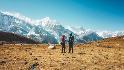 Obraz premium A couple walking on the Annapurna Circuit Trek, Himalayas, Nepal. Annapurna chain in the back, covered with snow. Clear weather, dry grass, snowy peaks. High altitude, man pointing to the peaks.