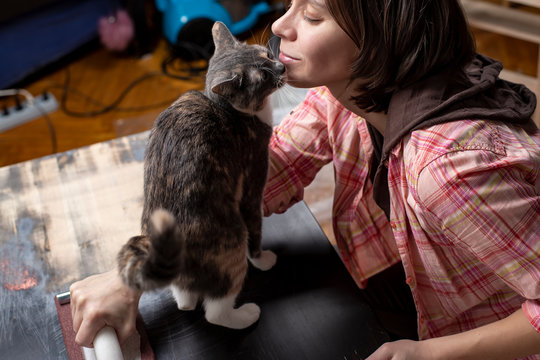 Woman prepares the surface for painting and sanding by hands an old wooden black table with a manual carpentry sandpapers holder, a beloved cat stands next to her and fondles her face. Home repairs.