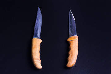 two knives with wooden handles are parallel, vertically on a black background