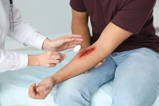 Female doctor cleaning young man's arm injury in clinic, closeup. First aid
