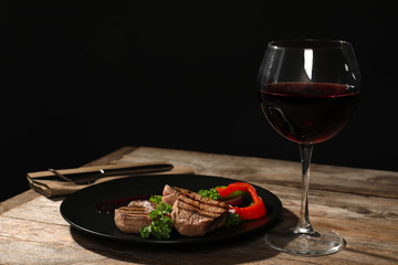 Grilled meat served with garnish and wine on table against black background. Space for text
