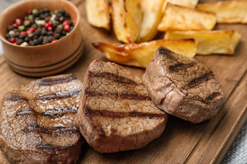 Grilled meat served with garnish on wooden board, closeup