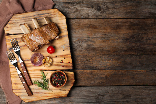 Flat lay composition with roasted ribs and space for text on wooden background. Tasty meat