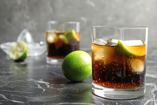 Glass of cocktail with cola, ice and cut lime on table. Space for text