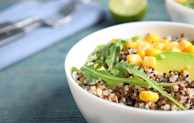 Healthy quinoa salad with vegetables in bowl on wooden table. Space for text