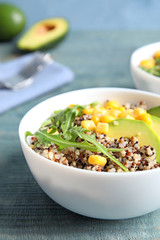 Healthy quinoa salad with vegetables in bowl on wooden table. Space for text