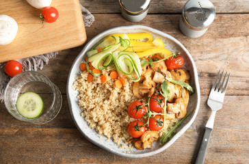 Plate with healthy quinoa salad and vegetables served on wooden table, top view