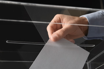 Man putting his vote into ballot box on black background, closeup