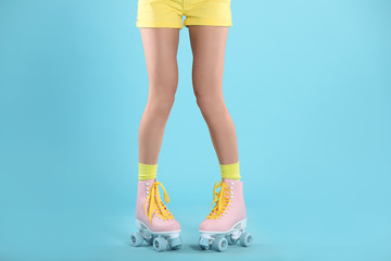Young woman with retro roller skates on color background, closeup