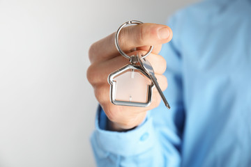 Naklejka premium Man holding house key with trinket on light background, closeup. Space for text
