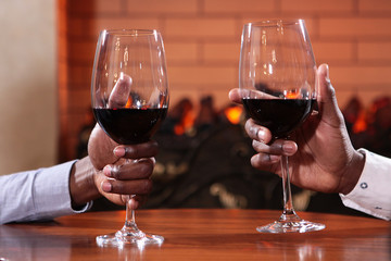Two hands of African Americans close - up with wine glasses on the table in the restaurant, on the background of the fireplace. The concept of the restaurant.