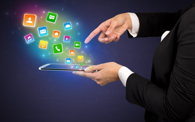 Hand holding tablet and application icons falling inwards
