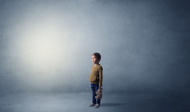 Little waggish kid staying alone in a big empty room with his plush
