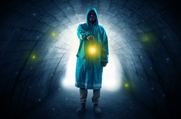 Fototapeta na wymiar Ugly man in raincoat walking with glowing lantern in a dark tunnel