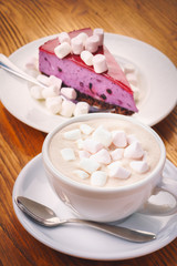 Cup of fresh hot chocolate drink with marshmallow and a piece of blueberry cake on the wooden table