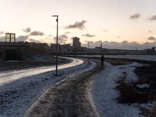 Snow-covered street in Reykjavik city. Reykjavik is the capital of Iceland. Photographed in October, in the evening. There's a person walking. In the background, there are buildings.