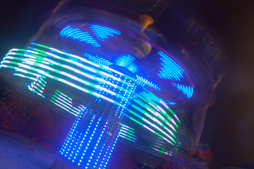 A blurry colorful carousel in motion at the amusement park, night illumination. The effect of bokeh and long exposure.