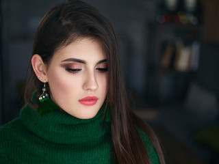 Fototapeta premium Dorywczo bliska portret szczęśliwa młoda brunetka kobieta modny makijaż zielony sweter i niestandardowe kolczyki pędzla.