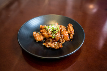 Sweet and Sour Chicken with sesame and green onions on the black plate on a Red wood table