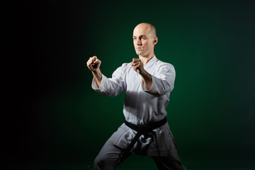 Adult athlete doing formal karate exercises on a dark green background