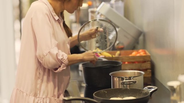 A mother mixes and stirs food with additional ingredients in the pot while it is on fire. She cooks lunch for her family. The background is blurred.