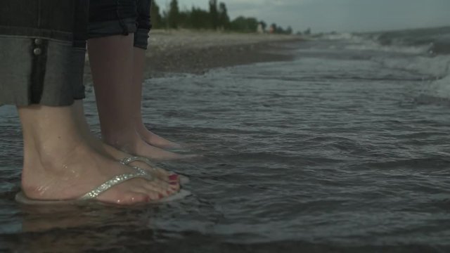 Two people's feet in water against crashing waves.