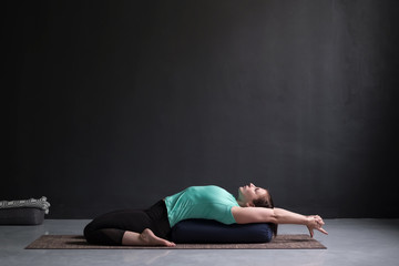 Fototapeta na wymiar Beautiful athletic girl doing yoga supta virasana asana using bolster