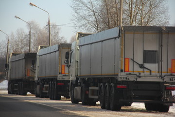 Three heavy trucks trucks with semi-trailers on roadside in winter day