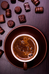 a cup of coffee and chocolate candies on a dark background.