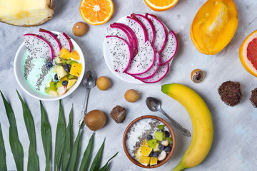 Breakfast table with yogurt acai bowls and fresh tropic fruits on a gray stone background with palm...