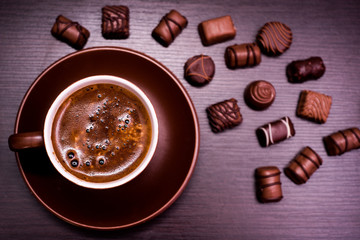 a cup of coffee and chocolate candies on a dark background.