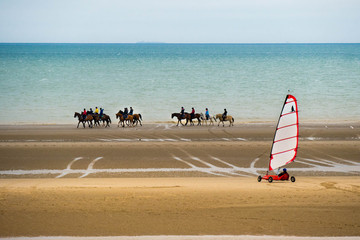 Plenty of horseback riders at the beach taking a ride with a sand yacht in the foreground