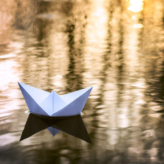 Small paper boat sailing down the river in Autumn at sunset. Concept of loneliness, abandonment,...