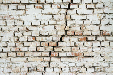 Brick wall with a big crack in the middle. Wall made of red brick and painted with white ink cracked vertically