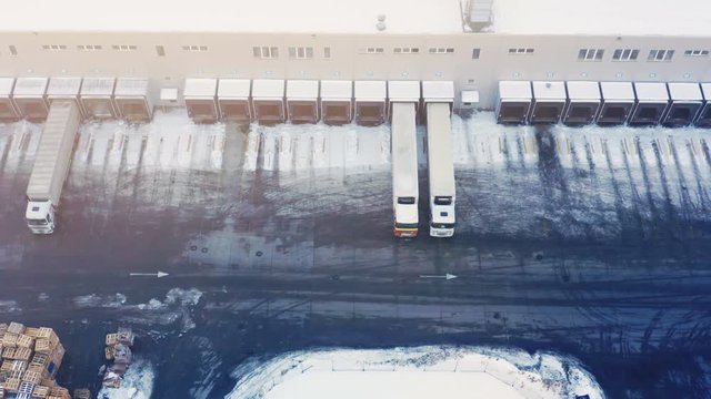 Aerial side view of a semi-trailers trucks standing at the ramps of a modern warehouse/ logistics hub on load/ unload goods